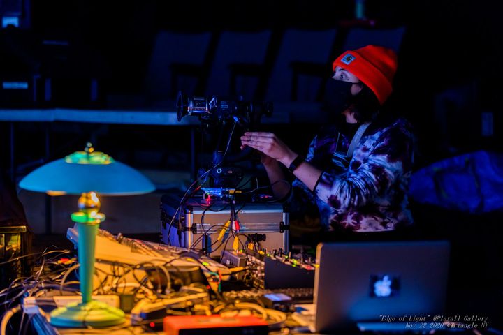 Paloma Kop performing at Edge of Light, sitting at a table covered with electronic equipment and wires