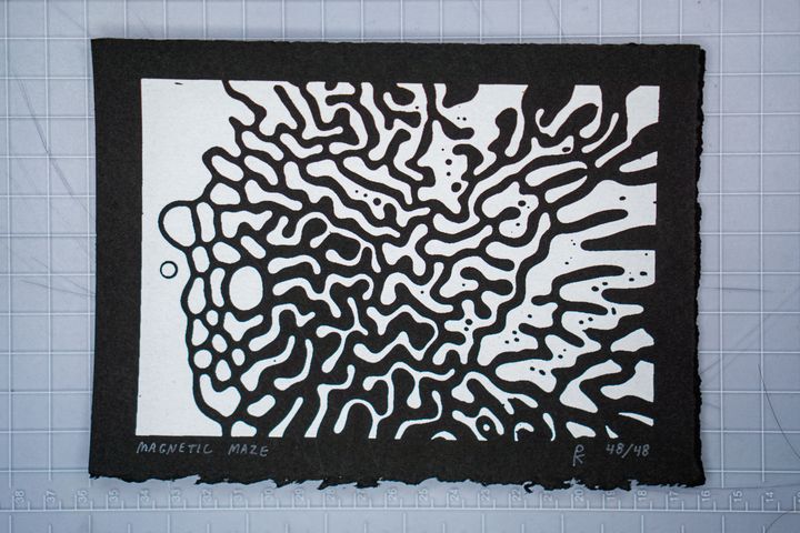 A silkscreen print of a maze-like pattern in white ink on black paper