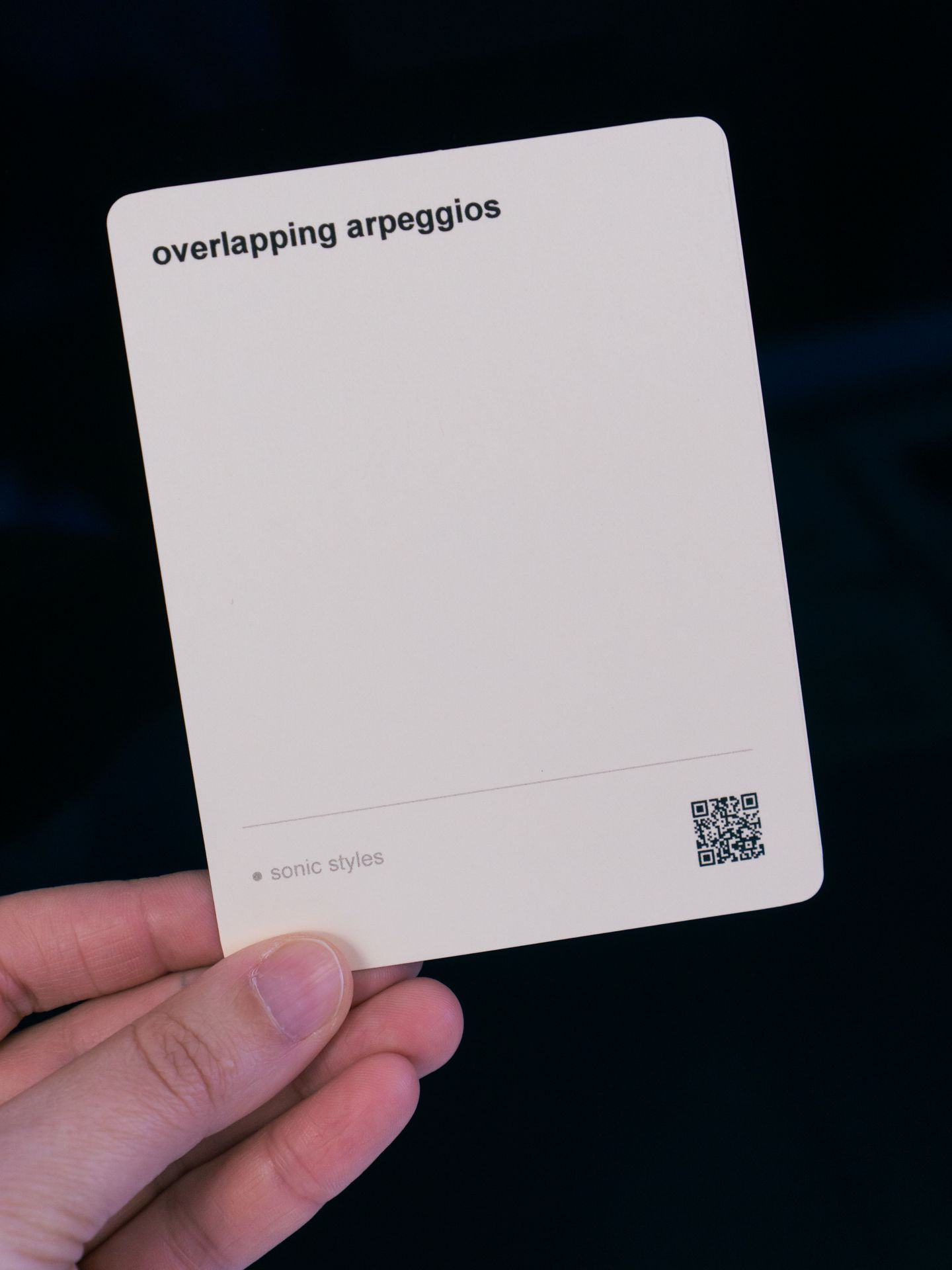 A hand holding up a single card with the text 'overlapping arpeggios'