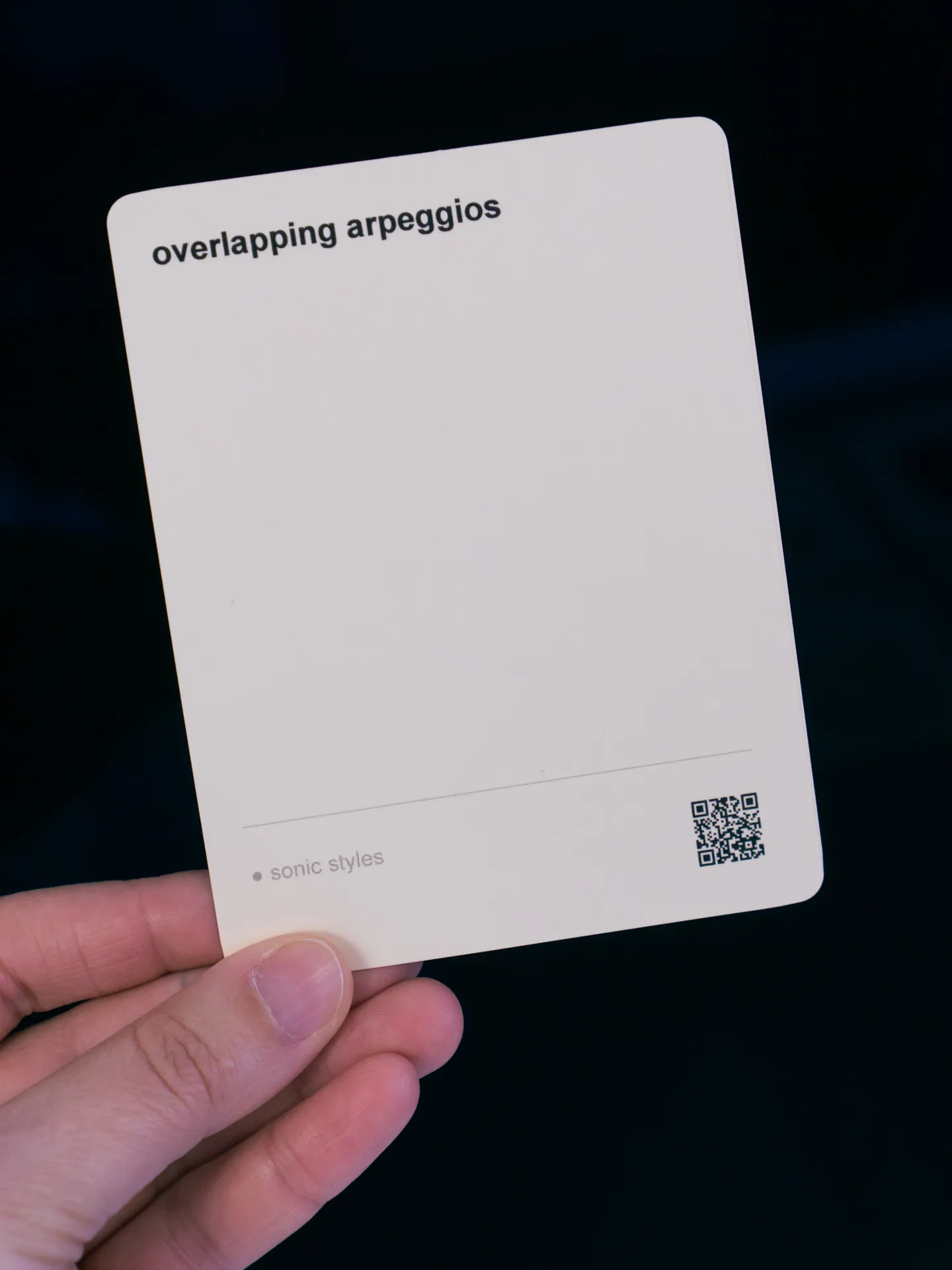 A hand holding up a single card with the text 'overlapping arpeggios'
