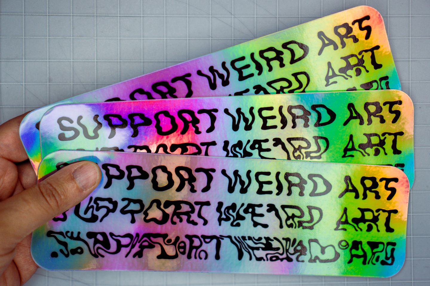 Holographic stickers with the text: Support Weird Art